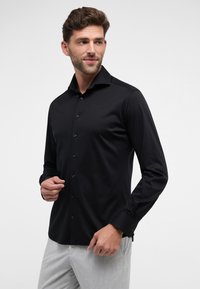 Schwarzes Langarmhemd aus glattem Stoff mit strukturiertem Kragen, vorderen Knöpfen und taillierter Passform. Minimalistischer Stil ohne Muster.