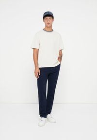Cotton short-sleeve t-shirt in cream with navy accents, paired with navy trousers and white sneakers, featuring a relaxed fit and simple design.