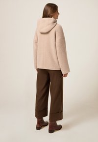 Chaqueta con capucha de textura beige y corte holgado, combinada con pantalones de pierna ancha marrón de estampado y botines marrón.