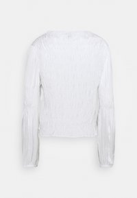 Blouse blanche à manches longues avec tissu froncé et manches légèrement bouffantes vue de dos sur un fond uni.
