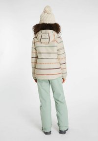 Puffjacke mit einer cremefarbenen Basis, die bunte geometrische Muster zeigt. Kombiniert mit mintgrünen Skihosen und einer strukturierten cremefarbenen Mütze.