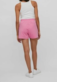 Rosa bomullsshorts med elastisk midja, designade för en avslappnad passform, tillsammans med en vit linne och vita sneakers.