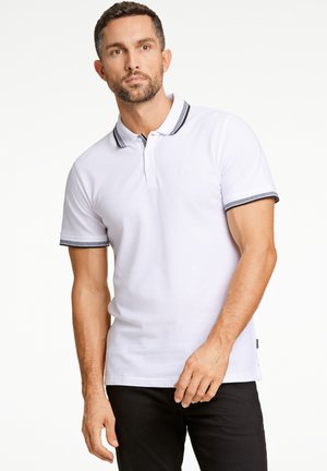 Camisa polo blanca con cuello, mangas cortas y acentos de rayas oscuras en el cuello y los puños. Textura de algodón suave.