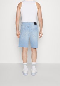 Vaaleansinisiä farkkushortseja, joissa on repaleinen helma; takataskut, joissa on ompeluyksityiskohtia; yhdistetty valkoisen hihattoman paidan ja vaaleapohjaisten tennareiden kanssa.