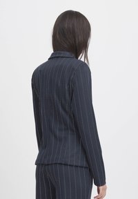 Marineblaue maßgeschneiderte Jacke mit vertikalen weißen Streifen, mit revers, langen Ärmeln und glatter Textur, von hinten gezeigt.