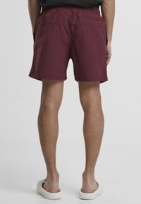 Burgunderfarbene Badehose aus leichtem Material mit einem elastischen Bund, seitlichen Taschen und einer Gesäßtasche zur Aufbewahrung.