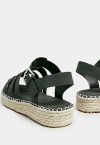 Sandali espadrille in pelle nera con fasce larghe, dettaglio fibbia e soletta in iuta. Suola sagomata per un comfort aggiuntivo.