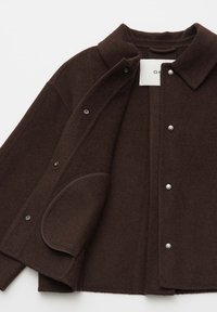 Veste en laine brun foncé avec fermeture à boutons-pressions, col à revers et poche plaquée arrondie, présentée partiellement ouverte sur un fond blanc.