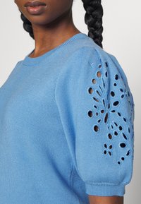 Maglione azzurro chiaro con scollo rotondo e design a maniche a sbuffo, caratterizzato da motivi floreali a occhio e tessuto a maglia testurizzato.