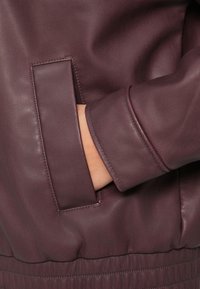 Giacca di pelle borgogna con tasca laterale e orlo arricciato. Texture liscia con polsini aderenti e dettagli di cucitura delicati.
