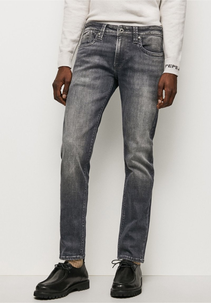 Mörkgrå denimjeans med rak benform, femfickorsdesign och subtila blekningar. Matchas med svarta skor och en ljus färgad tröja.