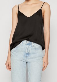 Top in raso nero con spalline sottili, scollo a V e fitting morbido, abbinato a jeans in denim azzurro chiaro a vita alta.