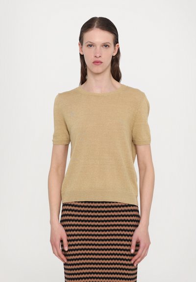 Kurzärmliger, runder Pullover in hellbeige mit weicher Textur. Kombiniert mit einem gemusterten Rock in Schwarz und Kupfer mit horizontalen Wellenlinien.