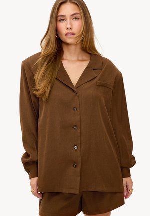 Camisa marrón de botones con cuello, mangas largas y un bolsillo en el pecho izquierdo. Acabado de tejido suave, corte relajado y textura blanda.