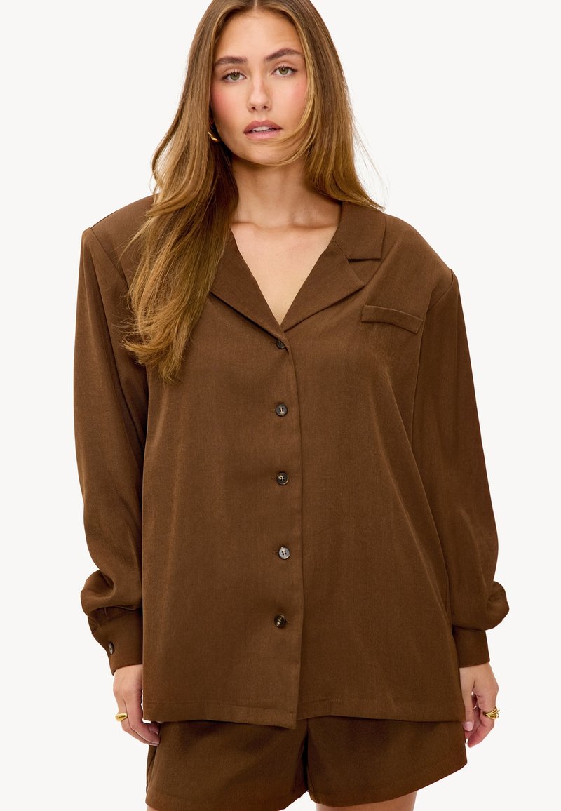 Chemise marron à boutons avec col, manches longues et poche plaquée sur la poitrine gauche. Finition en tissu lisse, coupe décontractée et texture douce.