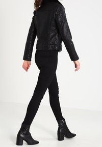 Černá kožená motorkářská bunda s přiléhavým střihem, spárovaná s černými skinny džínami a kotníkovými botami. Hladká textura, jednoduché kovové doplňky.