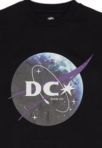 Schwarzes T-Shirt mit einem runden Grafikdesign, das einen blauen Planeten zeigt, lila Akzenten, "DC" in Weiß und Sternen auf einem strukturierten Hintergrund.