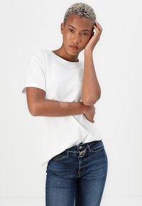 Witte katoenen T-shirt met ronde hals, korte mouwen, gecombineerd met donkerblauwe, slim-fit jeans met zilveren hardware en stikseldetails.