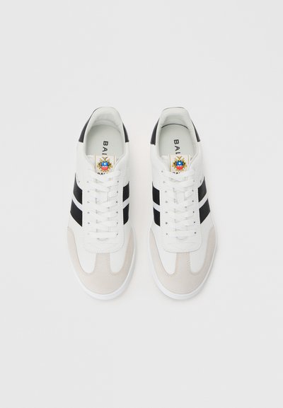 Adidași albi cu dungi negre, detalii din suede și un logo pe limbă. Prezintă un vârf rotunjit și o talpă plată din cauciuc.