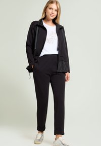 Giacca nera leggera con accenti grigi sopra una maglietta bianca con ricami floreali, abbinata a pantaloni neri affusolati e sneaker argentate.