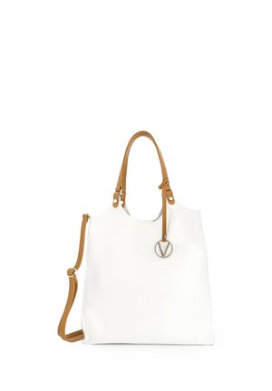 Hvid læder-totetaske med brune håndtag og justerbar skulderrem, med en rund sølvcharme fastgjort til det ene håndtag.