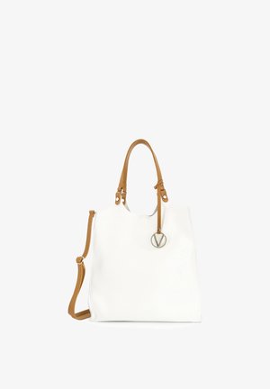 Witte leren totebag met lichtbruine handvatten en verstelbare schouderriem, met een ronde zilveren hanger bevestigd aan één handvat.