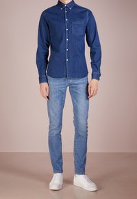 Mörkblå denimskjorta med knappar och bröstficka. Kombineras med ljusblå slim-fit jeans och vita sneakers. Slät textur, skräddarsydd passform.