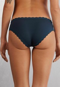 Marineblauwe katoenen slips met een geschulpt kant van de tailleband, voorzien van een gladde textuur en een lage pasvorm.