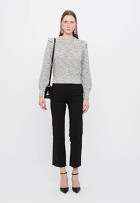 Un pull en maille grise avec un motif texturé et des épaules volantes, associé à un pantalon noir ajusté et des escarpins noirs, tenant un petit sac noir.