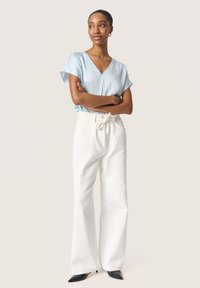 Blusa azzurro chiaro con maniche corte, caratterizzata da un collo a V, abbinata a pantaloni bianchi a gamba larga con texture e tacchi a punta neri.