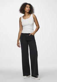 Weißes Rippen-Top mit Knopfdetails, kombiniert mit hoch taillierten schwarzen weit geschnittenen Jeans und schwarzen Sneakers mit weißen Sohlen.