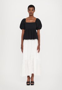 Zwarte top met pofmouwen en vierkante hals, gecombineerd met een witte, gelaagde maxi rok met bloemdetailing. Zwarte platform schoenen maken de look af.