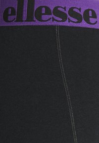 Svarta leggings med en bred lila elastisk midjeband som har texten "ellesse" i svart. Tyget har en slät struktur och minimal sömdetalj.