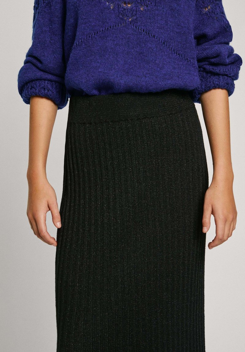 Falda negra de punto acanalado con una cintura ajustada, combinada con un suéter morado texturizado que cuenta con mangas enrolladas y patrones intrincados.