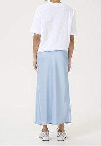 Weißes Baumwoll-T-Shirt mit kurzen Ärmeln kombiniert mit einem hellblauen, fließenden Midirock aus glattem Stoff, getragen mit grauen Sneakers.