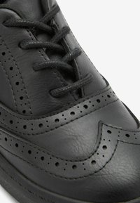 Svarta lädersneakers med en jämn yta, dekorativa perforeringar, rund tå och traditionellt snörningssystem.