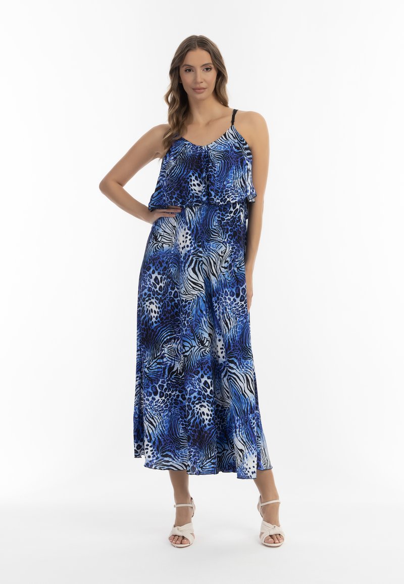 Rochie maxi cu imprimeu animalier albastru, cu un top stratificat cu volane, bretele subțiri și material fluid. Sandalele albe cu toc completează ținuta.