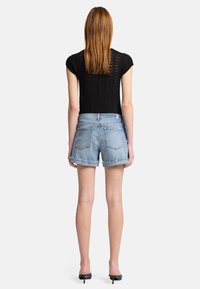 Szorty dżinsowe w jasnoniebieskim kolorze, z postrzępionym brzegiem, pięcioma kieszeniami i dopasowaną talią, zestawione z czarnym topem z koronki.