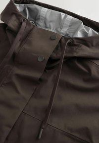 Capuche de veste imperméable marron foncé avec cordons ajustables, boutons-pression et doublure intérieure gris clair visible au niveau du col.
