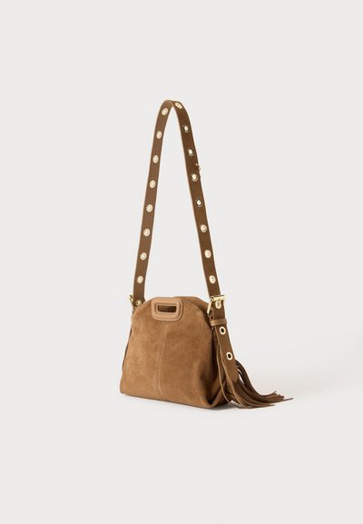 Sac bandoulière en daim marron avec une longue sangle réglable comportant des œillets métalliques ronds et un détail pompon sur le côté.