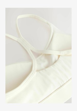 Gaiši krēmkrāsas sporta krūšturis ar gludu faktūru, kas piedāvā krustveida siksnas un elastīgas šuves atbalstam un komfortam.