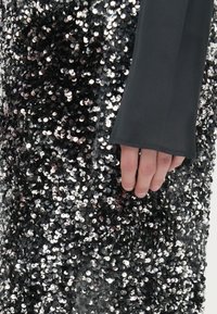 Abito nero con paillettes a forma circolare luccicanti, caratterizzato da un design aderente a maniche lunghe e un tessuto texturizzato.