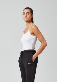 Witte, aangesloten tanktop met dunne bandjes, gecombineerd met zwarte loungebroeken met een trekkoord en een logo. Glad katoen, minimalistisch ontwerp.