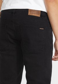 Jeans negre din denim, cu o etichetă din piele cu branding, cusături vizibile și două buzunare posterior cu un accent subtil al logo-ului.