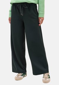 Pantaloni della tuta larghi di colore verde scuro con vita elasticizzata e cordoncino. Realizzati in tessuto morbido, presentano tasche laterali e gambe larghe.