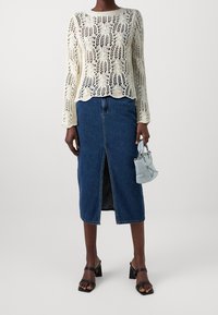 Háčkovaný krémový svetr s dlouhými rukávy, kombinovaný se sukní z denimu střední délky s předním rozparkem. Doplňkem je malá světle modrá kabelka.