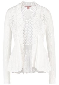 Vit kavaj med texturerad stickning och spetsdetaljer. Har öppen framsida, långa ärmar och peplum-siluett.