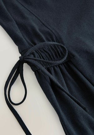 Dunkelblaues Gewebe mit einem gerafften Design und einem gebundenen Kordelzug. Weiche Textur und glatte Oberfläche, die einen lässigen, entspannten Stil unterstreicht.