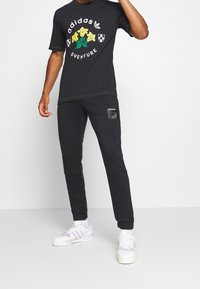 Černé tričko s krátkým rukávem se vzorem květin a potiskem loga. Doplněno černými zúženými tepláky s detaily na nášivce. Bílé tenisky.