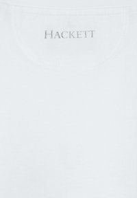Biely bavlnený tričko s okrúhlym výstrihom, na zadnej strane s nápisom "HACKETT" v jemnom šedom prešívaní. Hladká textúra.